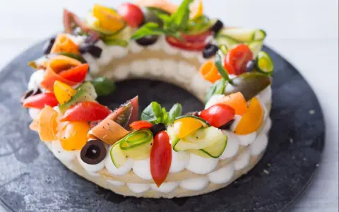 Deliciosa cream tart circular adornada con tomates, pepino, aceitunas y albahaca.