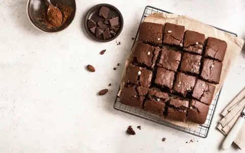 Delicioso brownie sin horno, cortado en cuadrados y espolvoreado con sal marina. Ingredientes como cacao y chocolate en trozos acompañan esta tentación.