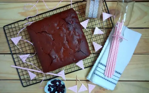 Un delicioso brownie recién horneado, listo para ser cortado. Decorado con banderines rosas y arándanos.
