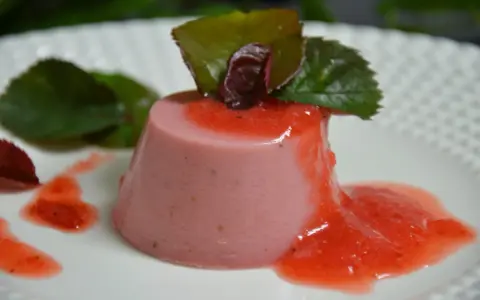 Delicioso panna cotta de fresa, bañado en salsa de fresa y decorado con hojas verdes.