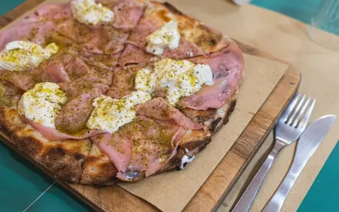 Pizza con mortadela y burrata cremosa, espolvoreada con hierbas verdes y servida en tabla de madera.