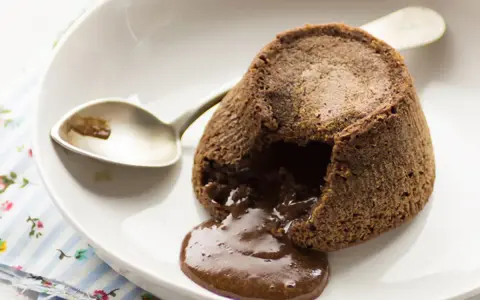 Coulant de chocolate recién horneado, con su interior líquido de chocolate derretido, listo para ser disfrutado con una cuchara.