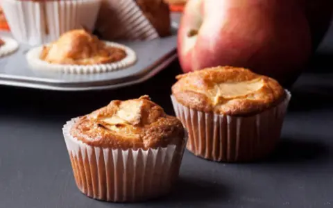 Dos deliciosos muffins de manzana recién horneados, con una manzana roja al fondo.
