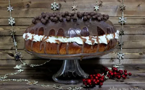 Un delicioso roscon de reyes chocolate, cubierto de glaseado y bolitas de chocolate, con crema y decoraciones navideñas.
