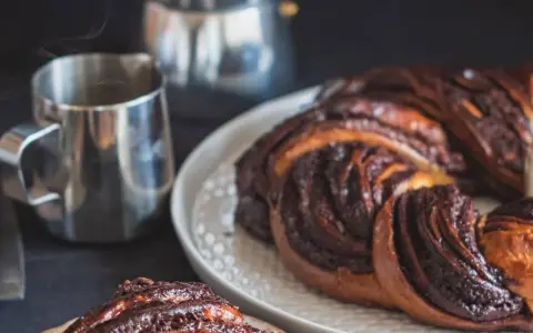 Deliciosa trenza de chocolate recién horneada, humeante junto a una taza de café.