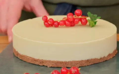 Deliciosa tarta de chocolate blanco, decorada con grosellas rojas y una hoja de menta.