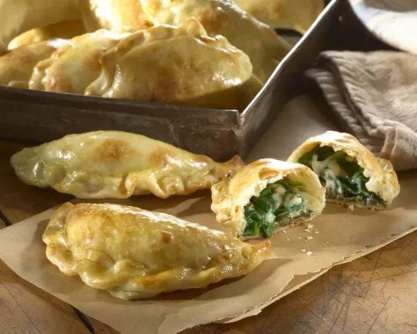 Empanadillas de espinacas y queso recién horneadas, doradas y crujientes, con un relleno cremoso y sabroso.