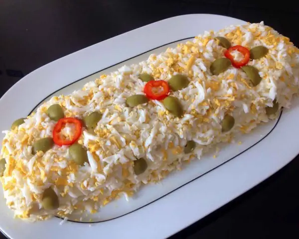 Brazo de gitano de patata cubierto de huevo duro rallado, aceitunas verdes y rodajas de pimiento rojo.