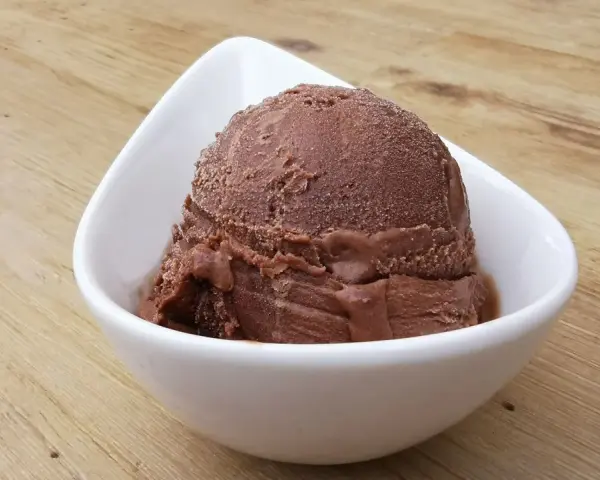Cremoso helado de platano y chocolate en un cuenco blanco sobre una mesa de madera.