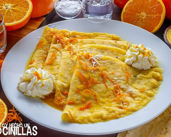 Crepes Suzette, cubiertos con ralladura de naranja y servidos con crema batida.