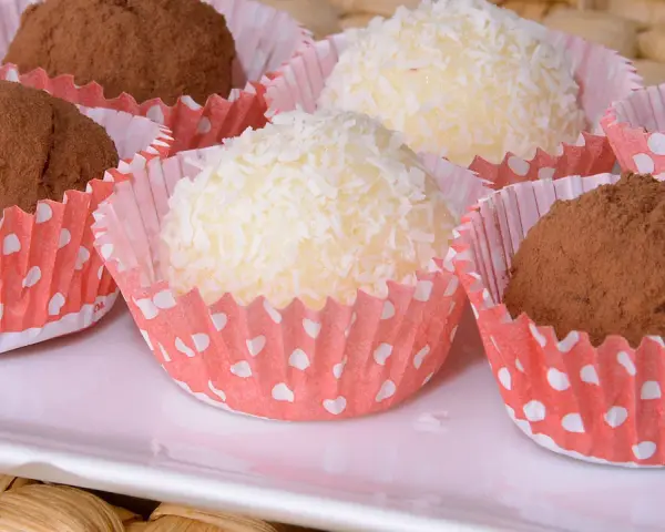 Deliciosas trufas de coco y chocolate, algunas cubiertas de coco rallado y otras de cacao en polvo, presentadas en capacillos rojos con puntos blancos.