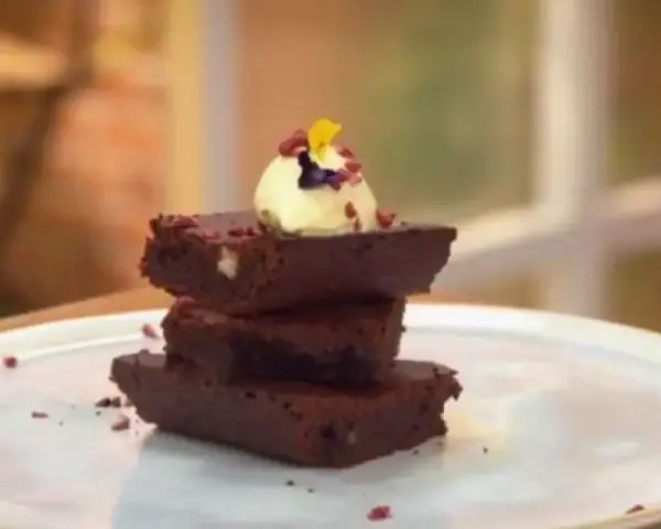 Delicioso brownie airfryer apilado, coronado con helado y pétalos.