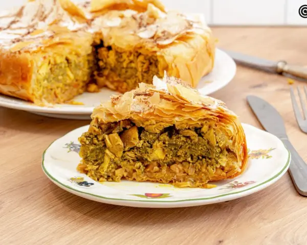 Pastela marroqui, un pastel salado de hojaldre relleno de pollo y especias, servido en un plato decorado.