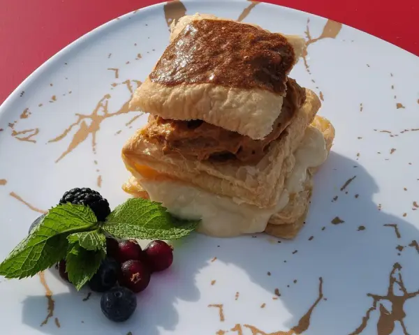 Delicioso postre de milhojas de crema, con capas crujientes y relleno dulce, acompañado de frutos rojos y menta fresca.