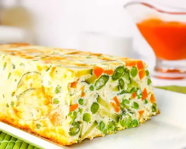 Pastel de verduras casero, con guisantes, zanahoria y calabacín, servido en un plato blanco.