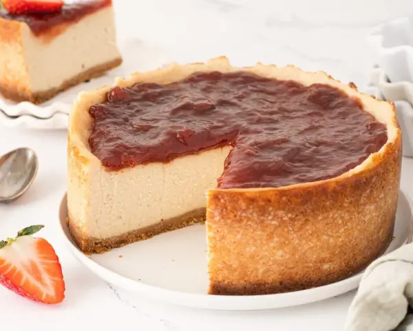 Tarta de queso vegana con cobertura de fresa, cremosa y deliciosa. Una porción ya cortada muestra su interior.