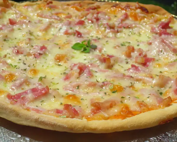 Pizza con masa hecha en Thermomix, cubierta de queso fundido, trocitos de bacon y hierbas aromáticas.