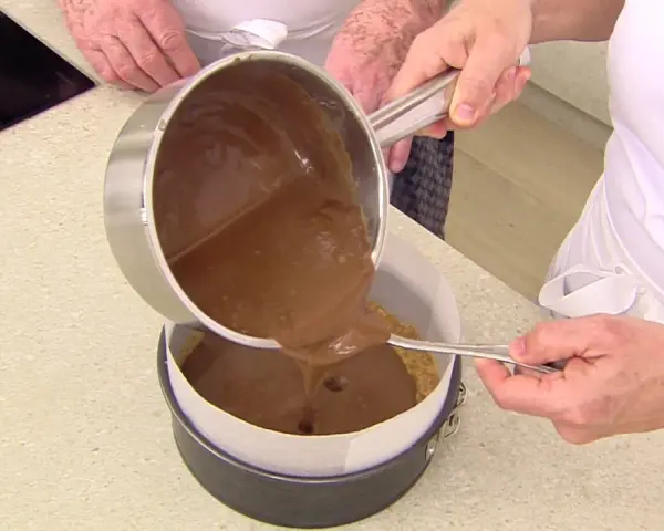 Vertiendo cobertura de chocolate sobre una base de galleta para un delicioso pastel de chocolate.