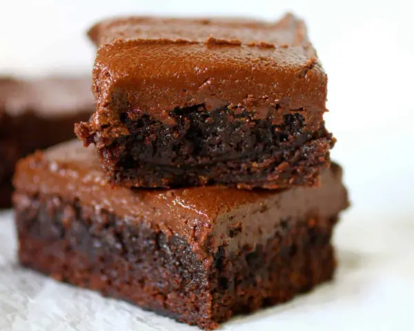 Dos deliciosos brownies con nueces apilados, cubiertos con glaseado de chocolate cremoso.