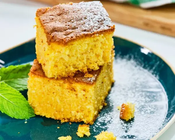 Dos porciones de bizcocho de calabaza, espolvoreadas con azúcar glas, junto a hojas de menta fresca en un plato azul.