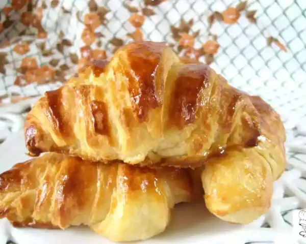 Dos croissants caseros dorados y brillantes, apilados en un plato blanco.