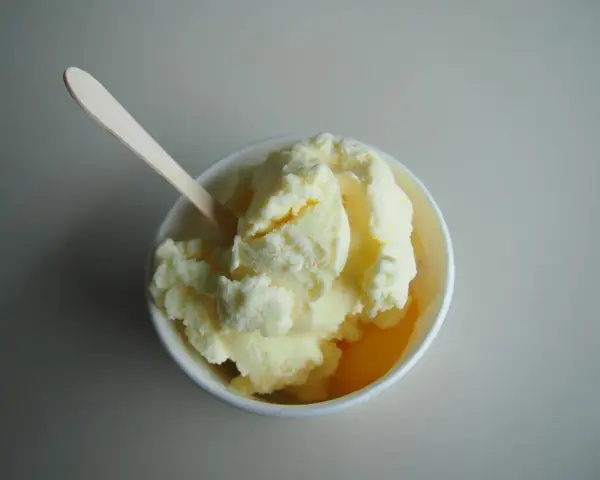 Un cremoso helado de melón en un cuenco blanco, listo para ser disfrutado con su cuchara de madera.