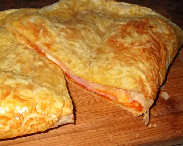 Empanada de jamón y queso dorada, con queso gratinado y relleno jugoso. ¡Un bocado delicioso!