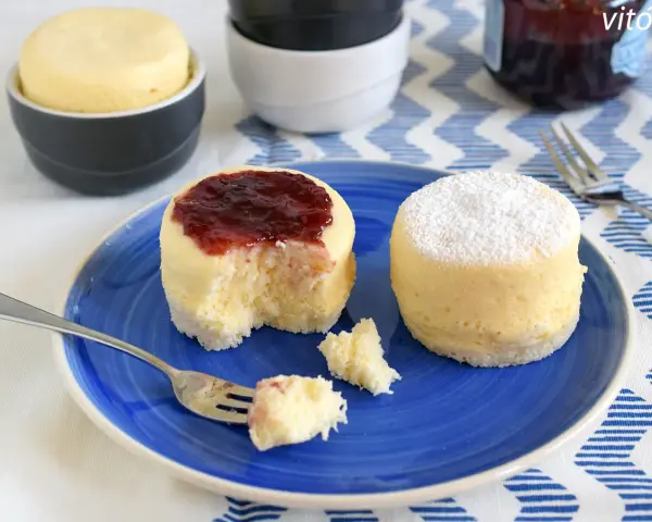 Dos bizcochos de microondas en un plato azul. Uno tiene mermelada de fresa y el otro azúcar glas.
