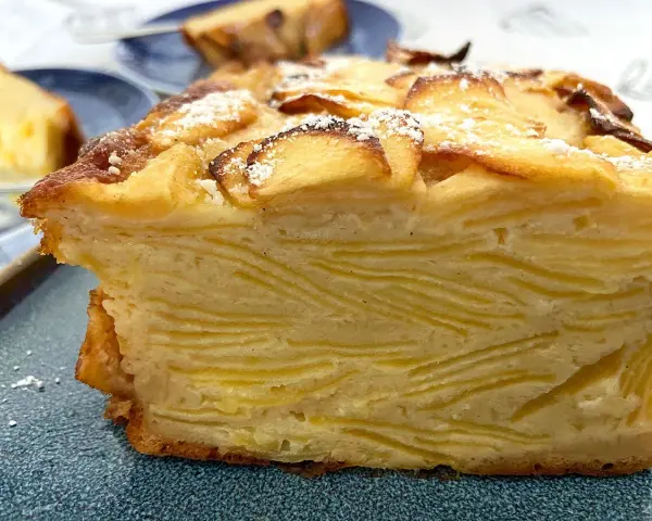Un trozo de pastel de capas con trozos de manzana en la parte superior, espolvoreado con azúcar glas. Un postre invisible aux pommes.