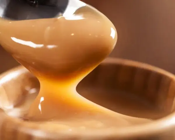 Cuchara vertiendo manjar blanco cremoso en un cuenco de madera.