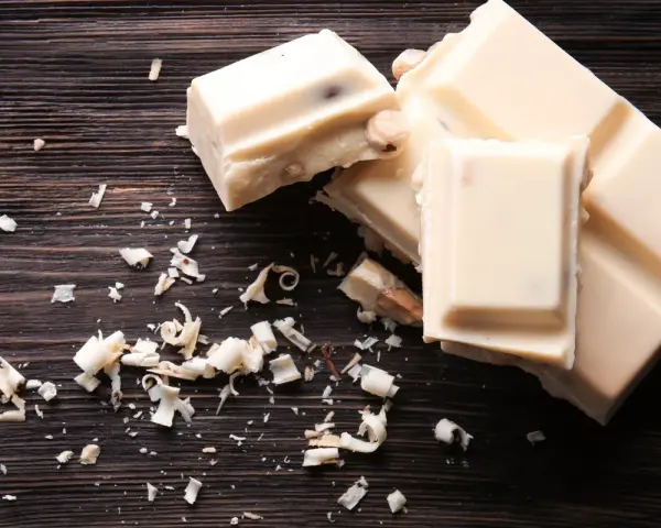 Deliciosos postres con chocolate blanco, trozos y virutas esparcidos sobre una tabla de madera oscura.