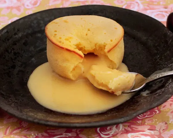 Coulant de chocolate blanco con interior cremoso, servido en plato negro con cerezas.