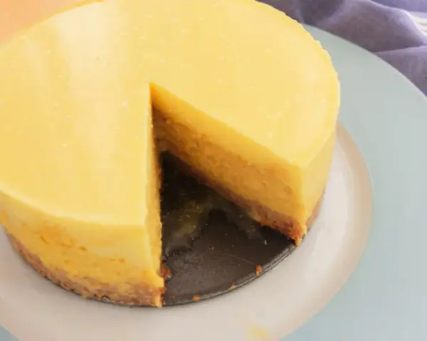 Tarta mango cremosa, con una porción retirada, sobre plato azul claro.