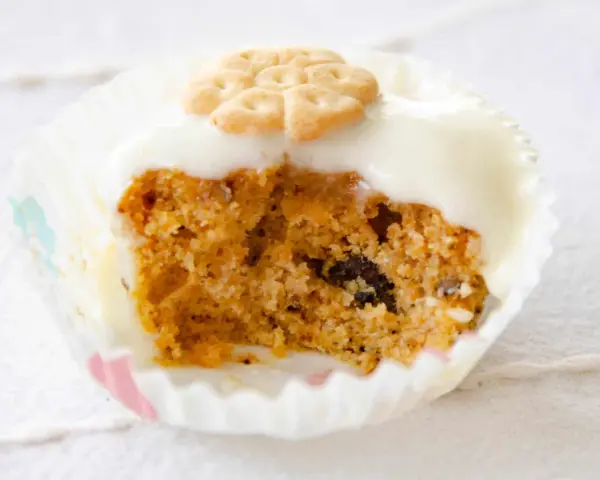 Un muffin de zanahoria con glaseado blanco y una galleta decorativa en forma de flor.