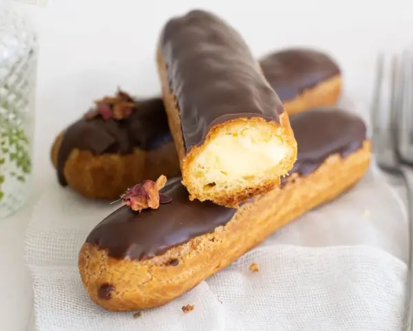 Pastel eclair cubierto de chocolate, relleno de crema. Decorado con pétalos secos.