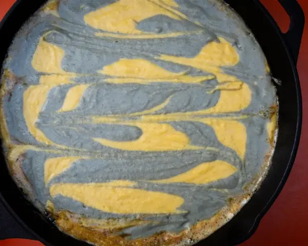 Pastel de maíz con remolinos grises y amarillos en una sartén de hierro fundido.