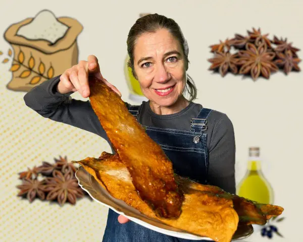 Mujer sonriente muestra una coca de vidre dorada, con ingredientes como harina, anís y aceite de oliva de fondo.