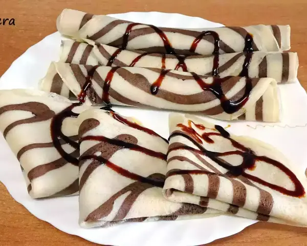 Deliciosos crepes de chocolate rayados, enrollados y doblados, cubiertos con sirope de chocolate.