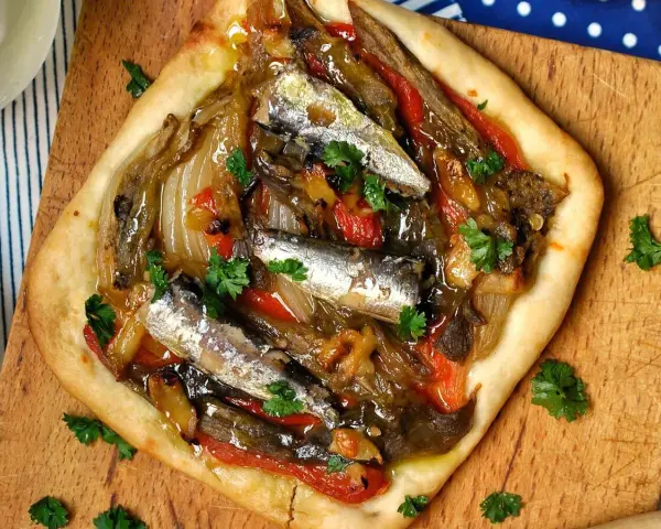Coca de recapte con verduras asadas y sardinas, decorada con perejil fresco.
