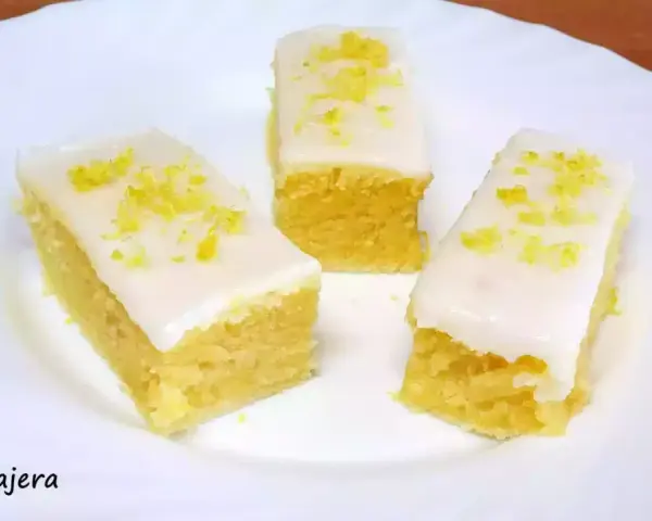 Tres porciones de brownie de limón con glaseado blanco y ralladura de limón, servidas en un plato blanco.