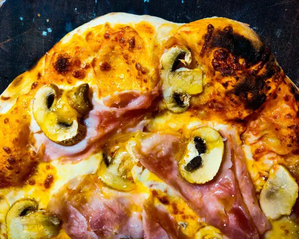 Pizza masa madre con champiñones y jamón, con bordes dorados y burbujas de queso fundido.