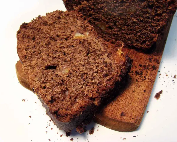 Rebanadas de pan de chocolate húmedo y denso, con trozos de fruta confitada, servidas en una tabla de madera.