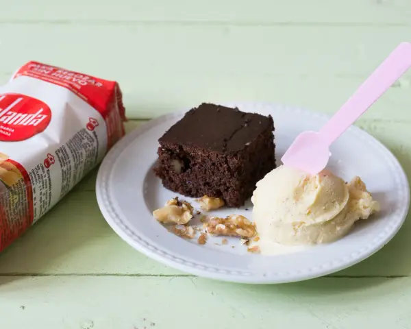 Un delicioso brownie sin huevo con helado de vainilla y nueces, junto a un paquete de Yolanda.