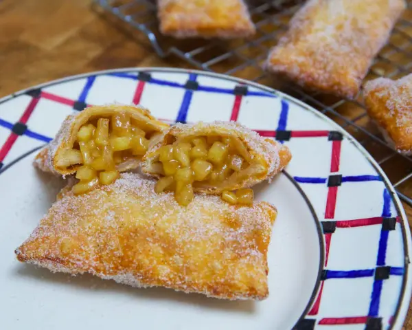 Empanada de manzana recién hecha, dorada y espolvoreada con azúcar. Una está partida, mostrando el relleno jugoso de manzana.