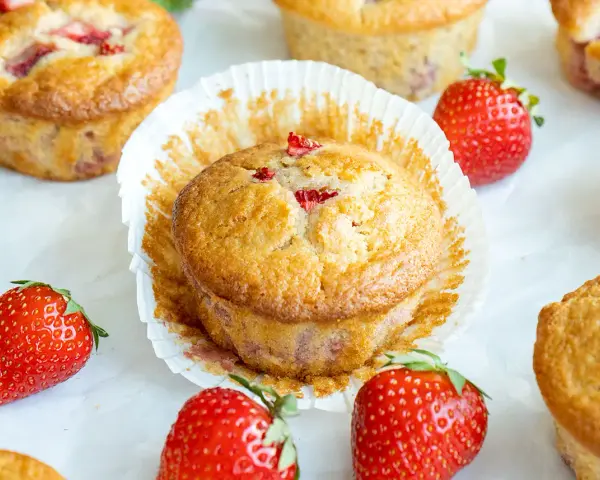 Delicioso postre con fresas, muffins dorados con trozos de fresa y fresas frescas alrededor.