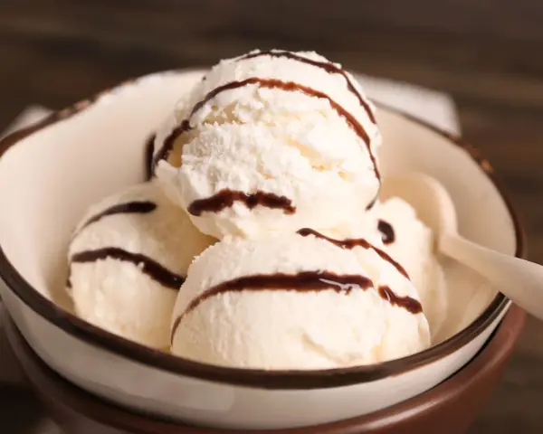 Cuatro bolas de helado de chocolate blanco con sirope de chocolate en un cuenco.