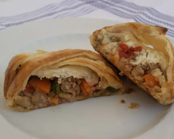 Hojaldre con carne picada y verduras, cortado por la mitad, mostrando el relleno jugoso.