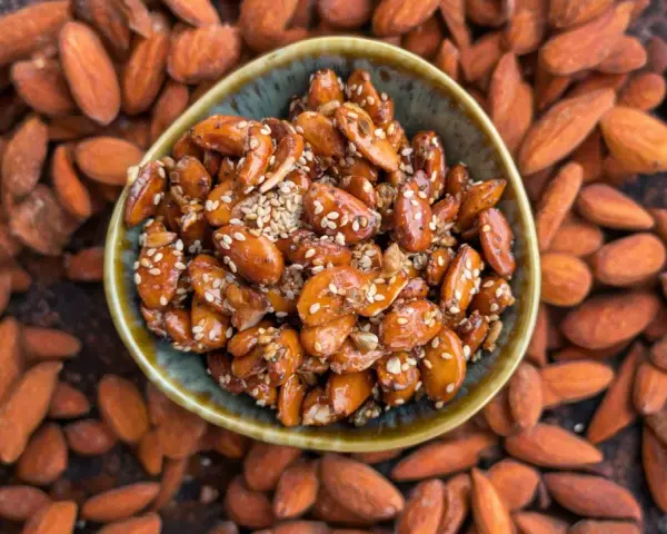 Un cuenco lleno de almendras caramelizadas, cubiertas de semillas de sésamo, rodeadas de almendras enteras.