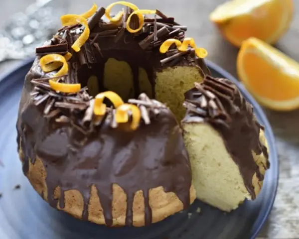 Bizcocho de chocolate y naranja, cubierto con glaseado de chocolate, virutas de chocolate y cáscara de naranja.