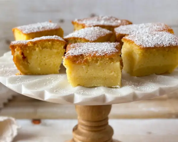 Porciones de un pastel mágico, cubiertas con azúcar glas, sobre un soporte de mármol.